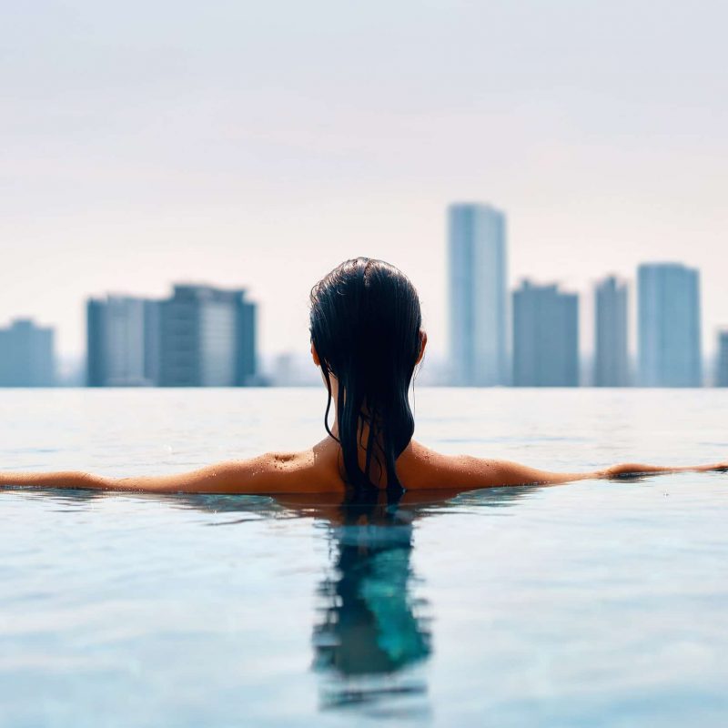 Beautiful woman in rooftop pool overlooking cityscape